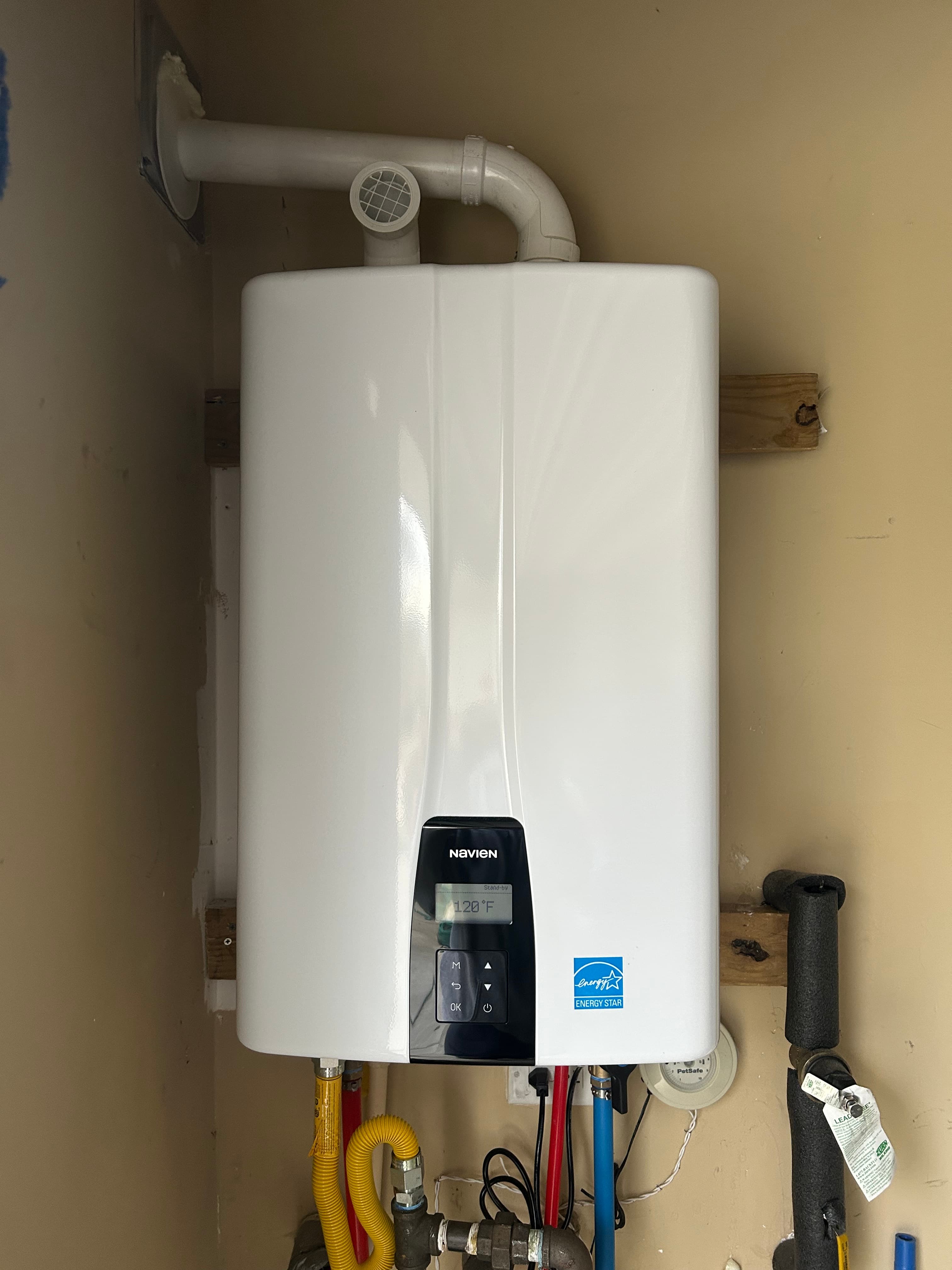 Wall-mounted Navien tankless water heater with a digital display and various colored utility pipes.