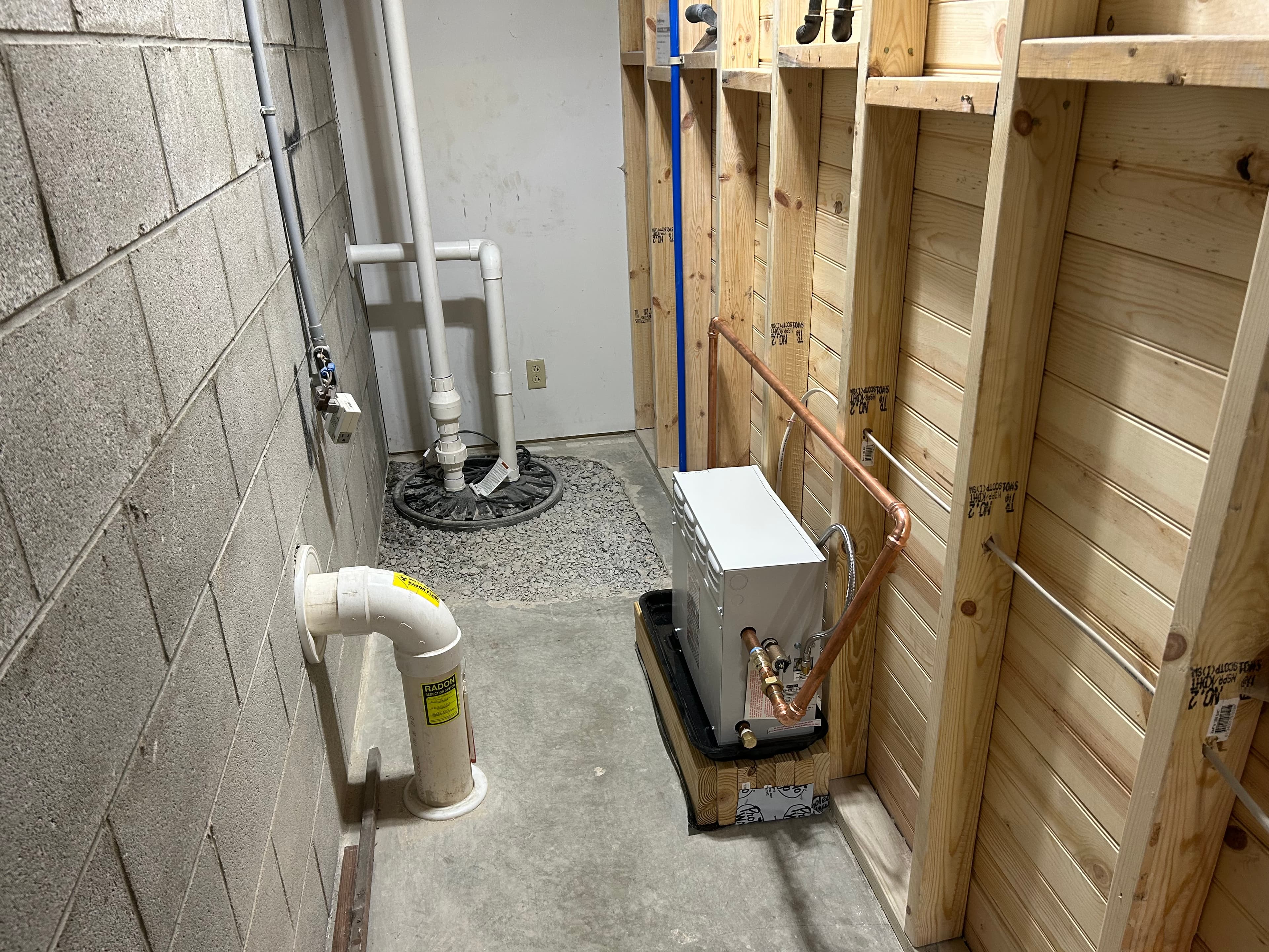 Unfinished basement utility room with radon pipe, sump pump, and heater with copper pipes.