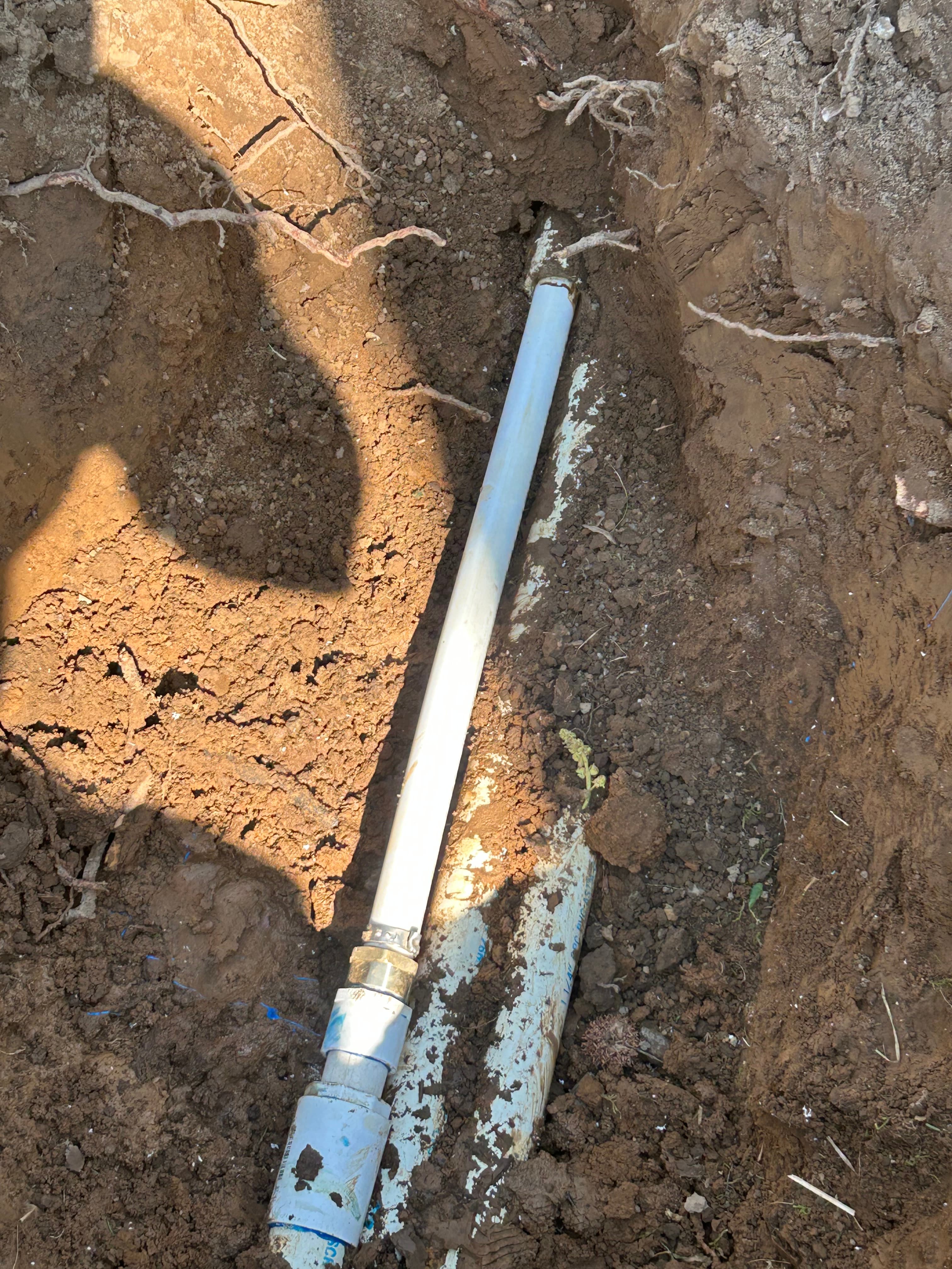 White PVC pipe with a metal coupling installed in an excavated dirt trench for repair.
