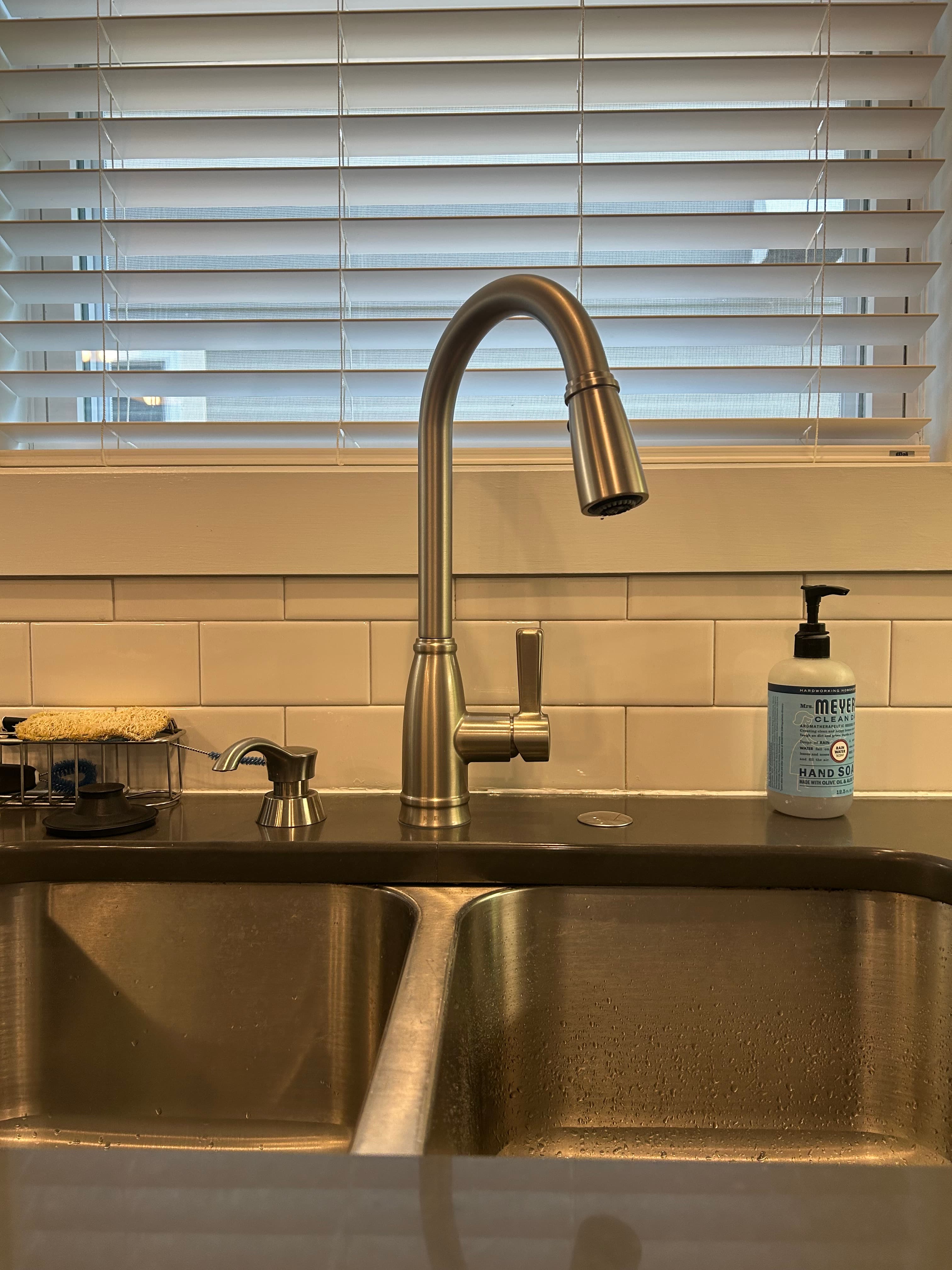 Brushed nickel gooseneck faucet over a stainless steel double sink with white subway tile backsplash.