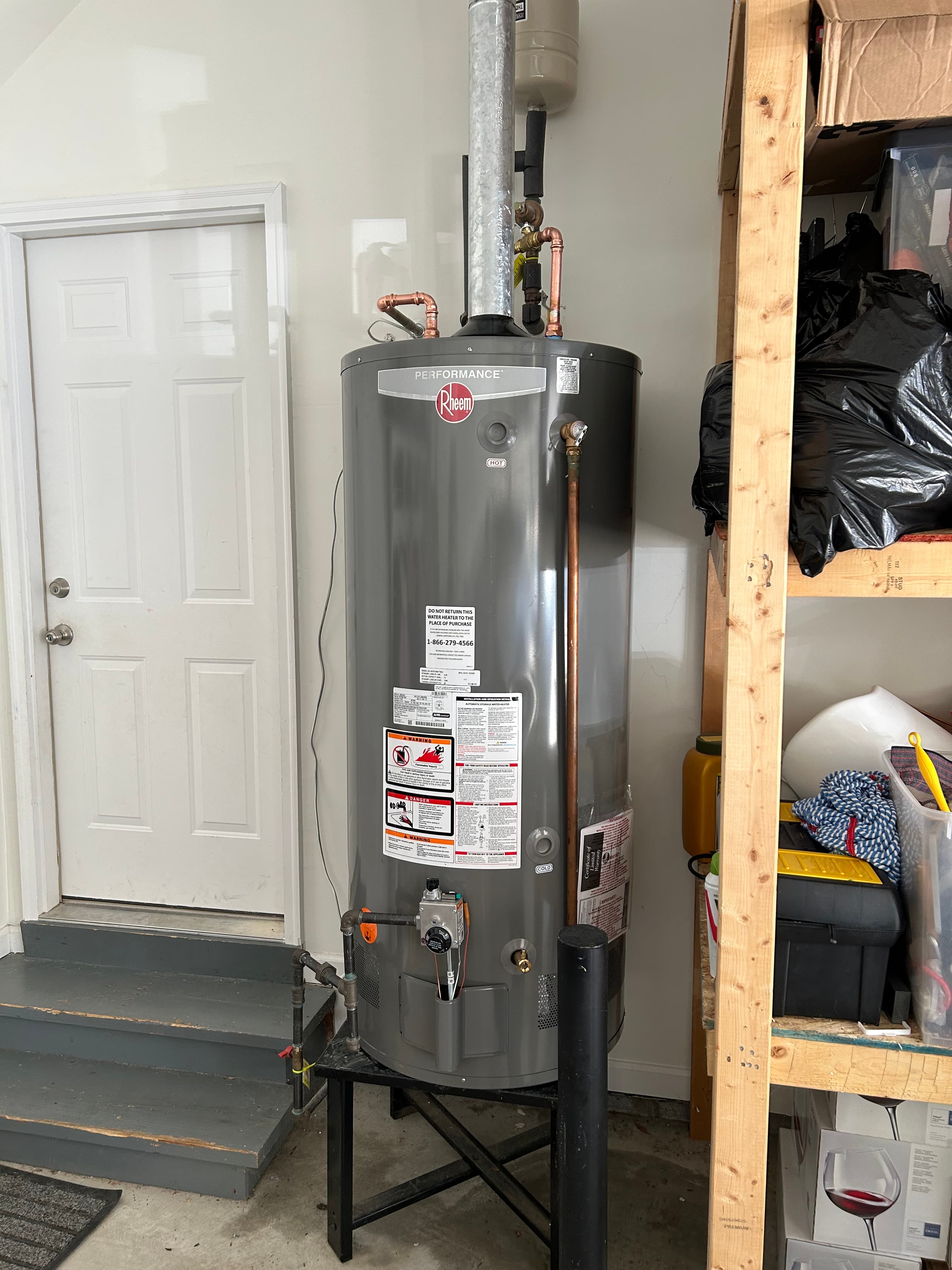 Grey Rheem Performance gas water heater on a black stand in a garage utility area.