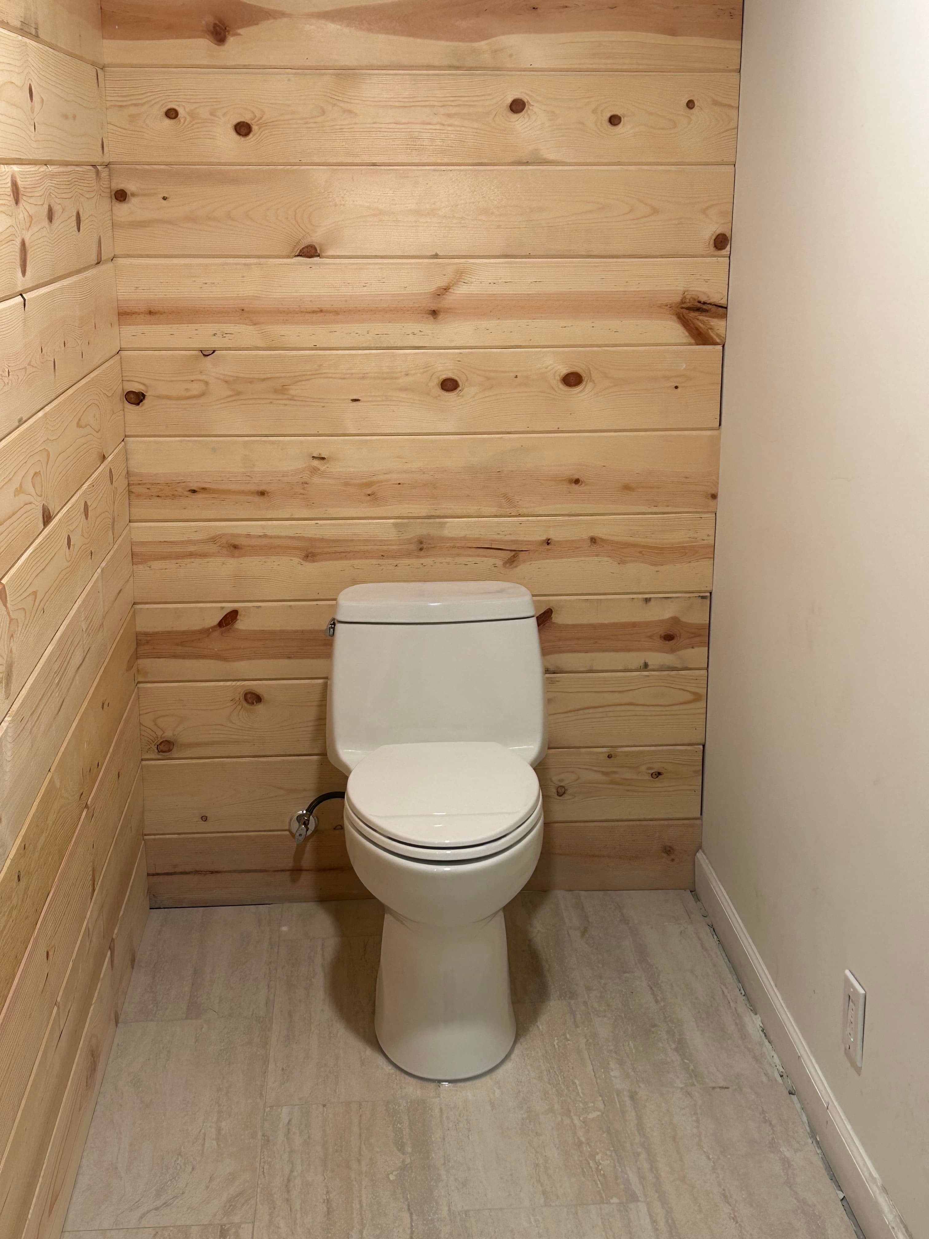 White toilet centered against a light wood plank wall in a small, modern bathroom.