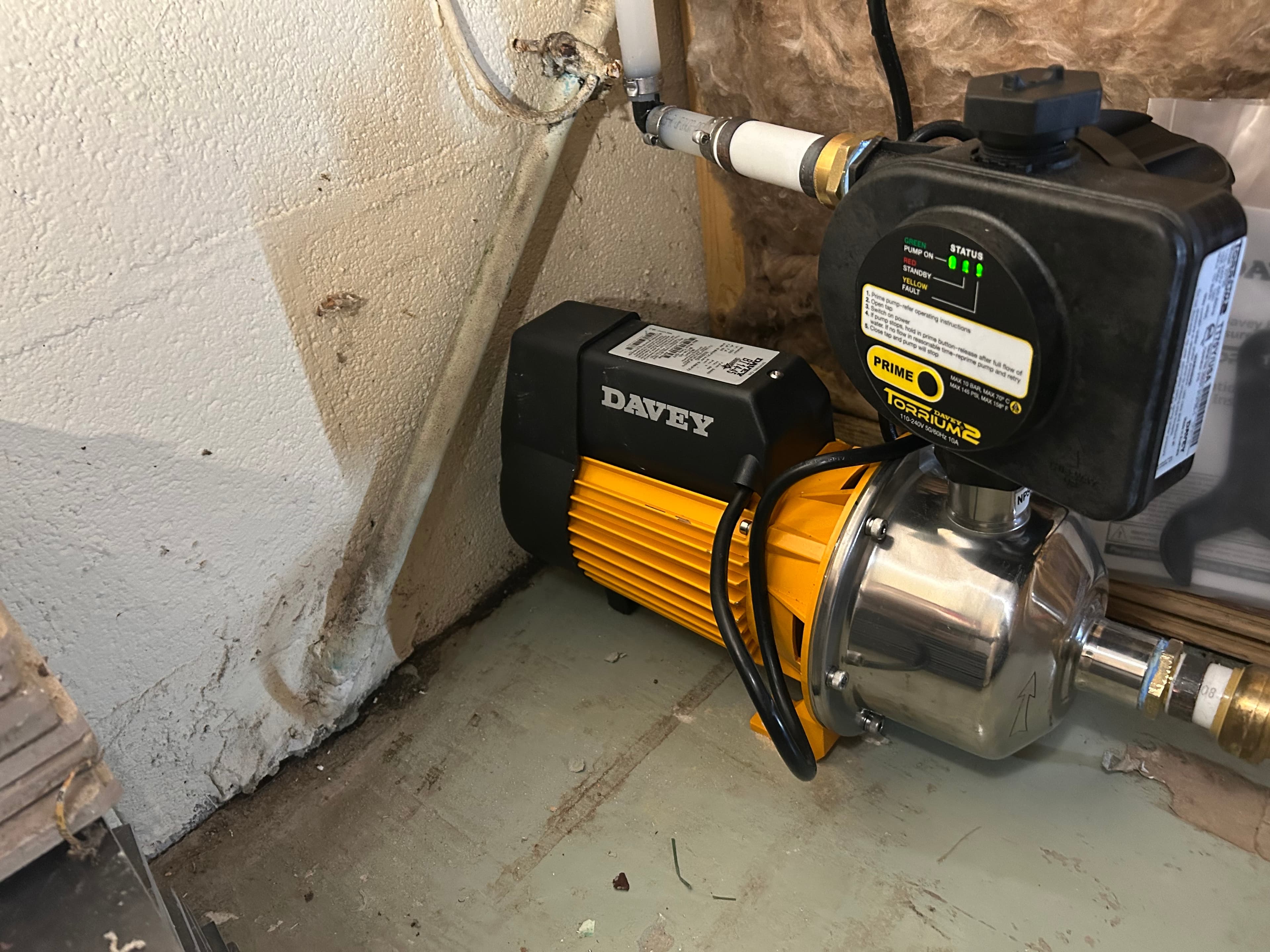 Yellow and black Davey water pump with a Torrium2 controller installed against a concrete wall.