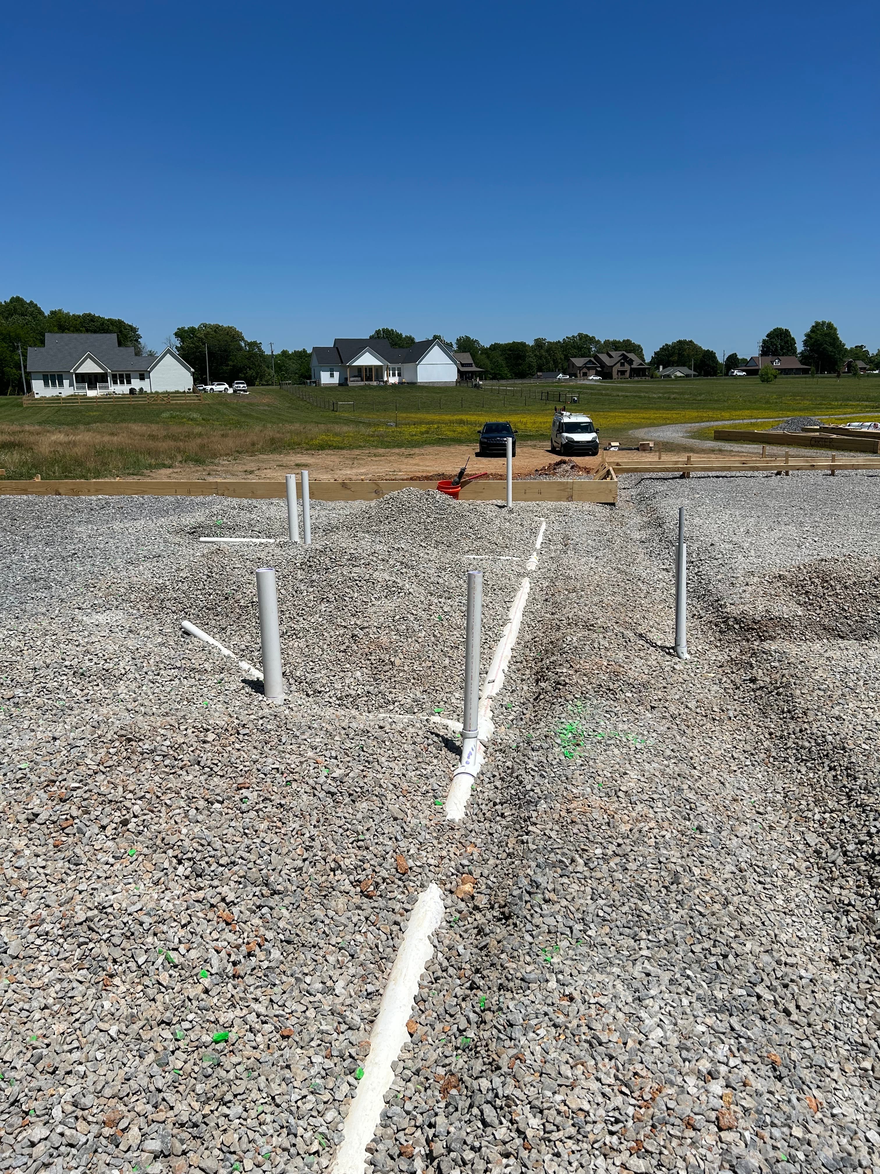 White PVC plumbing pipes installed in a gravel foundation at a residential construction site.