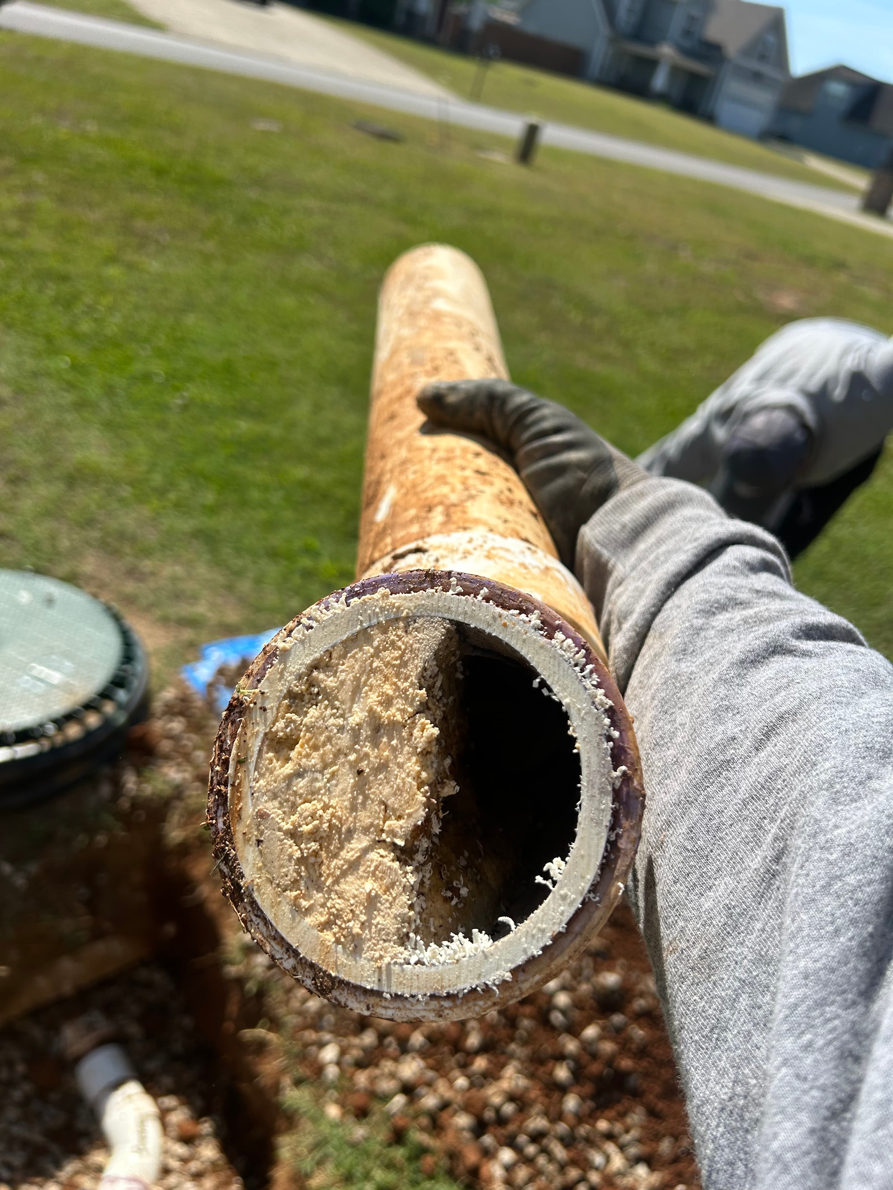 A gloved hand holds a rusty pipe nearly completely blocked by thick, beige grease buildup.