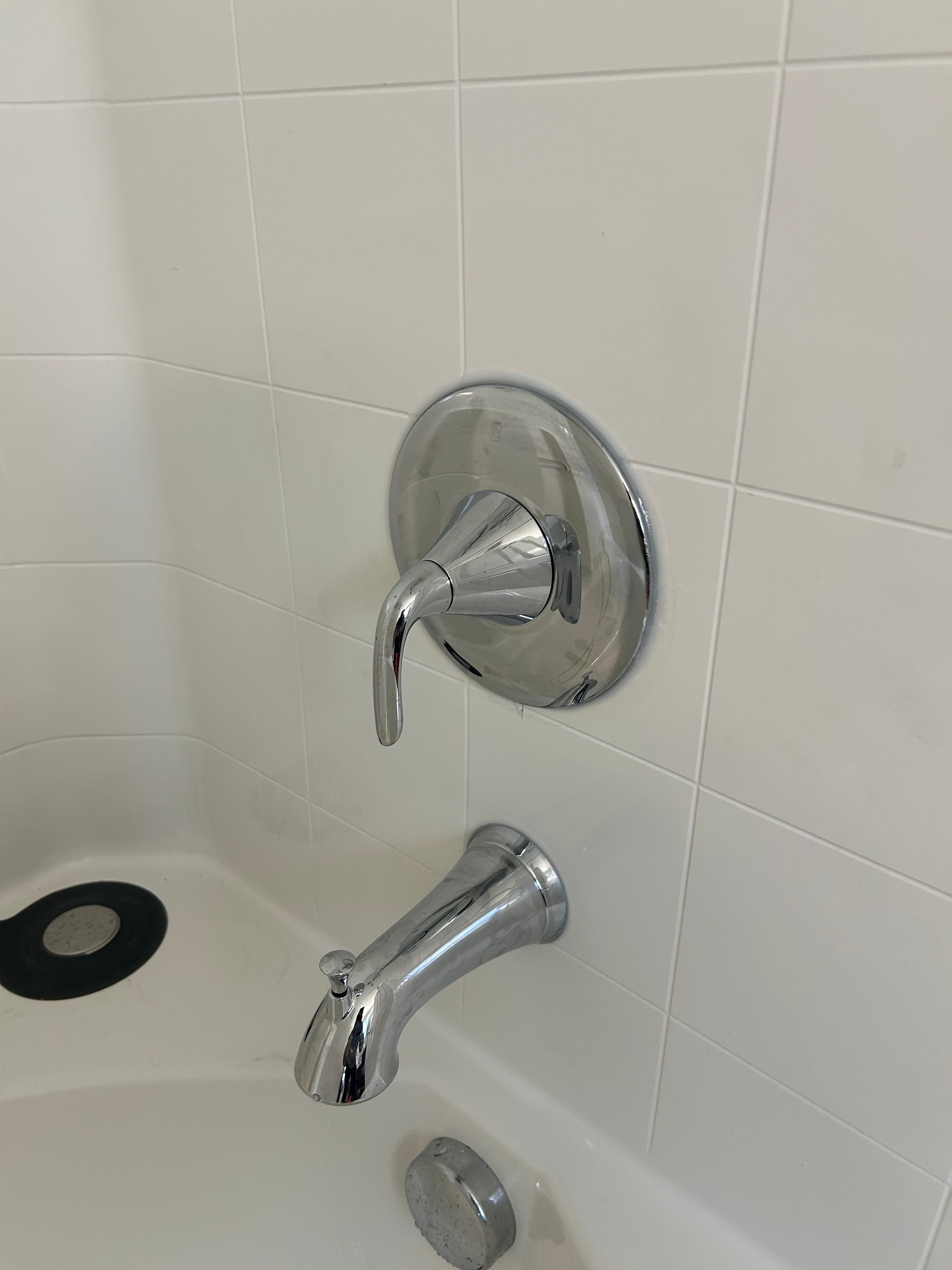 Polished chrome shower handle and tub spout mounted on a white tiled bathroom wall.