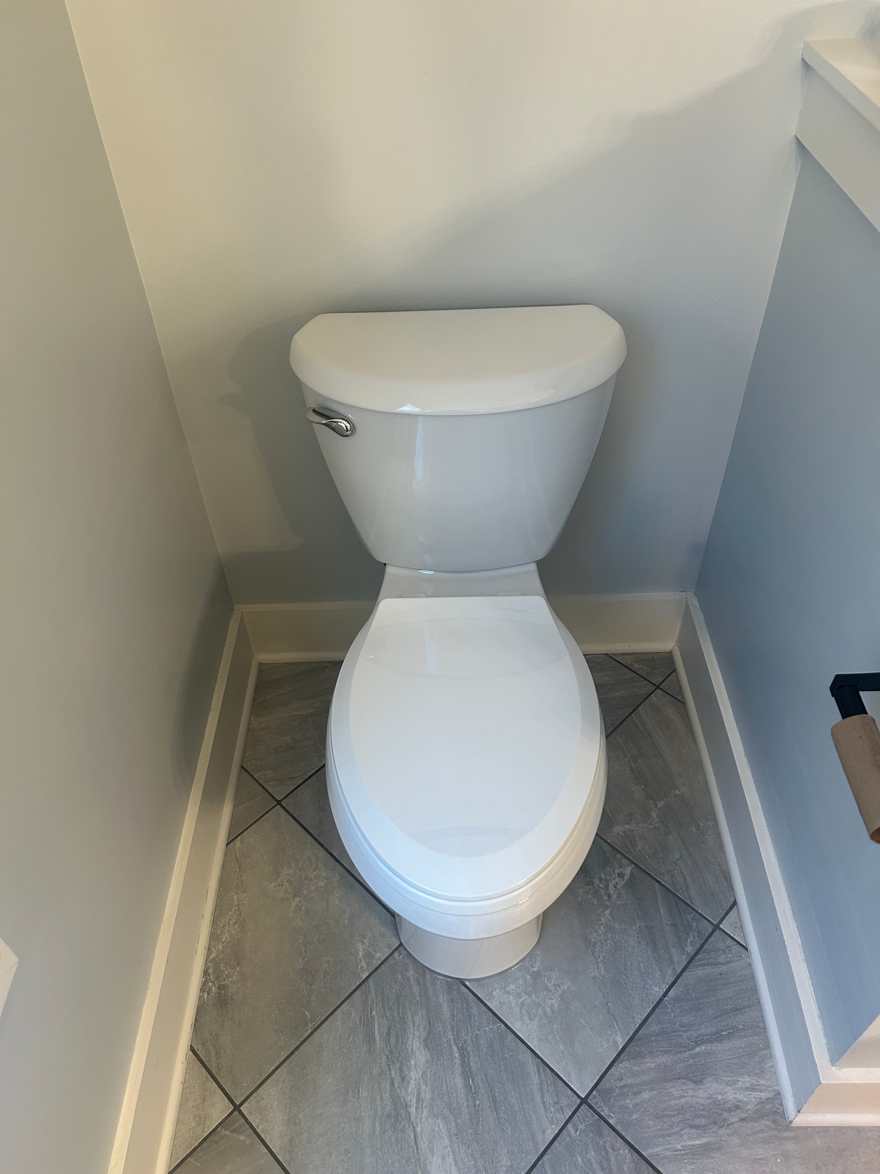 White ceramic toilet with a closed lid on grey diagonal floor tiles in bathroom.