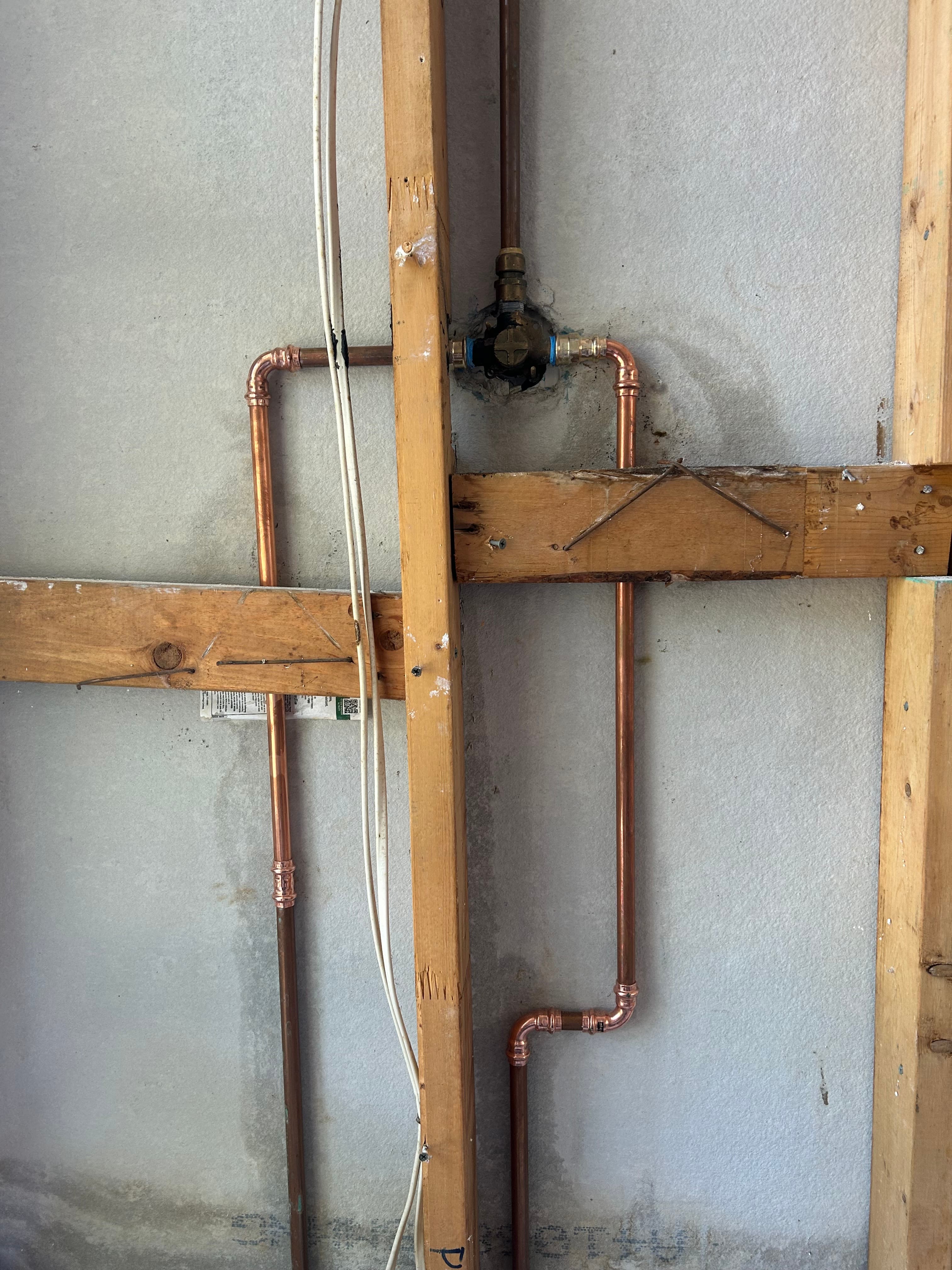 Copper pipes and a brass valve installed in a wooden wall frame against concrete.