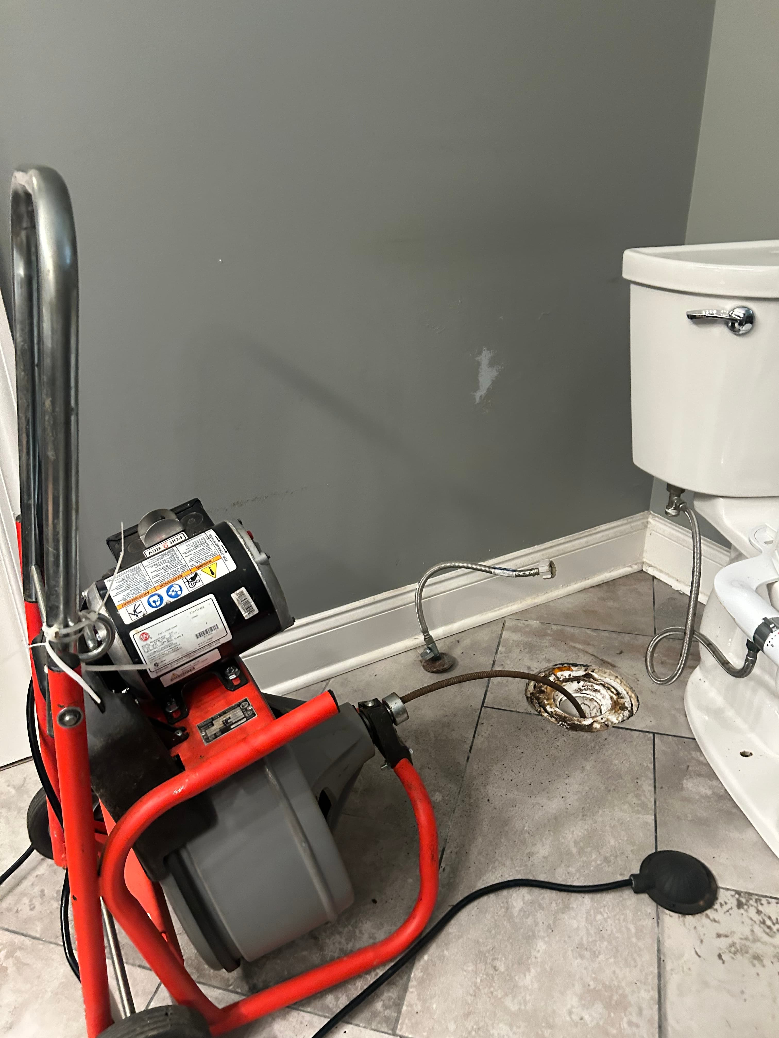 Red plumbing snake machine with cable inserted into an open toilet floor drain flange.