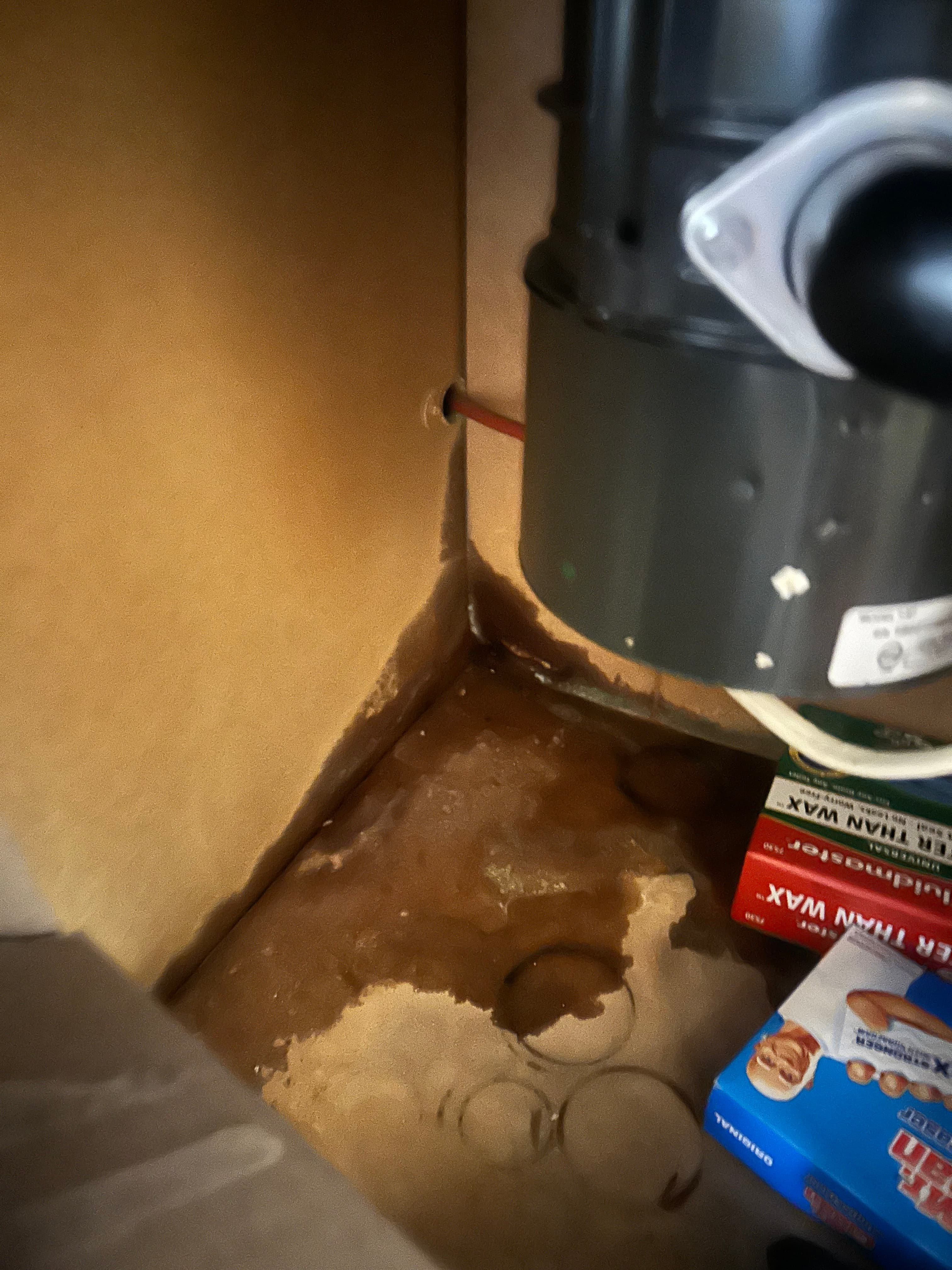 Large dark water stain and pooling liquid on the bottom of a kitchen cabinet under a sink.