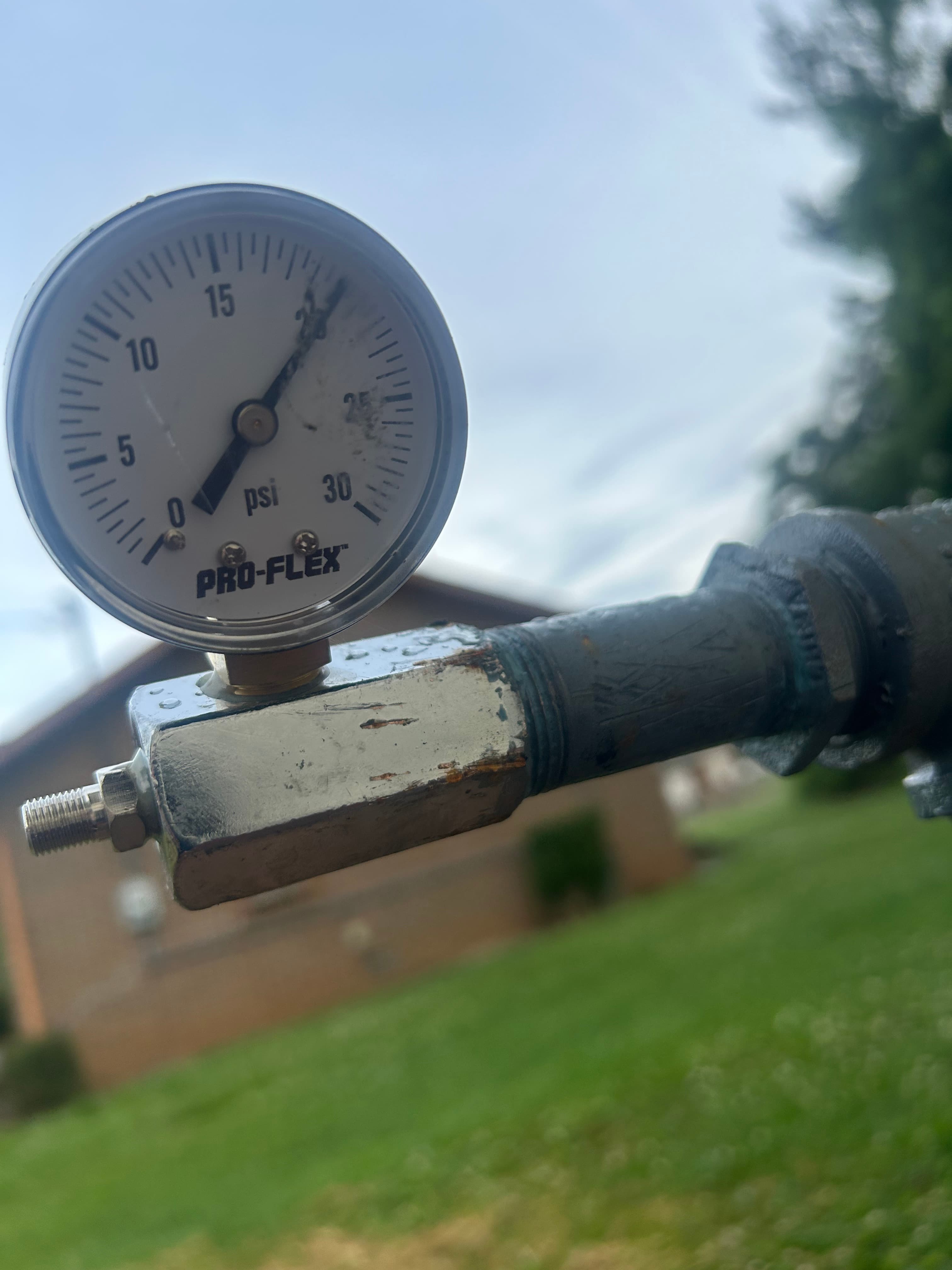 PRO-FLEX pressure gauge reading about 22 psi, attached to an outdoor metal pipe assembly.