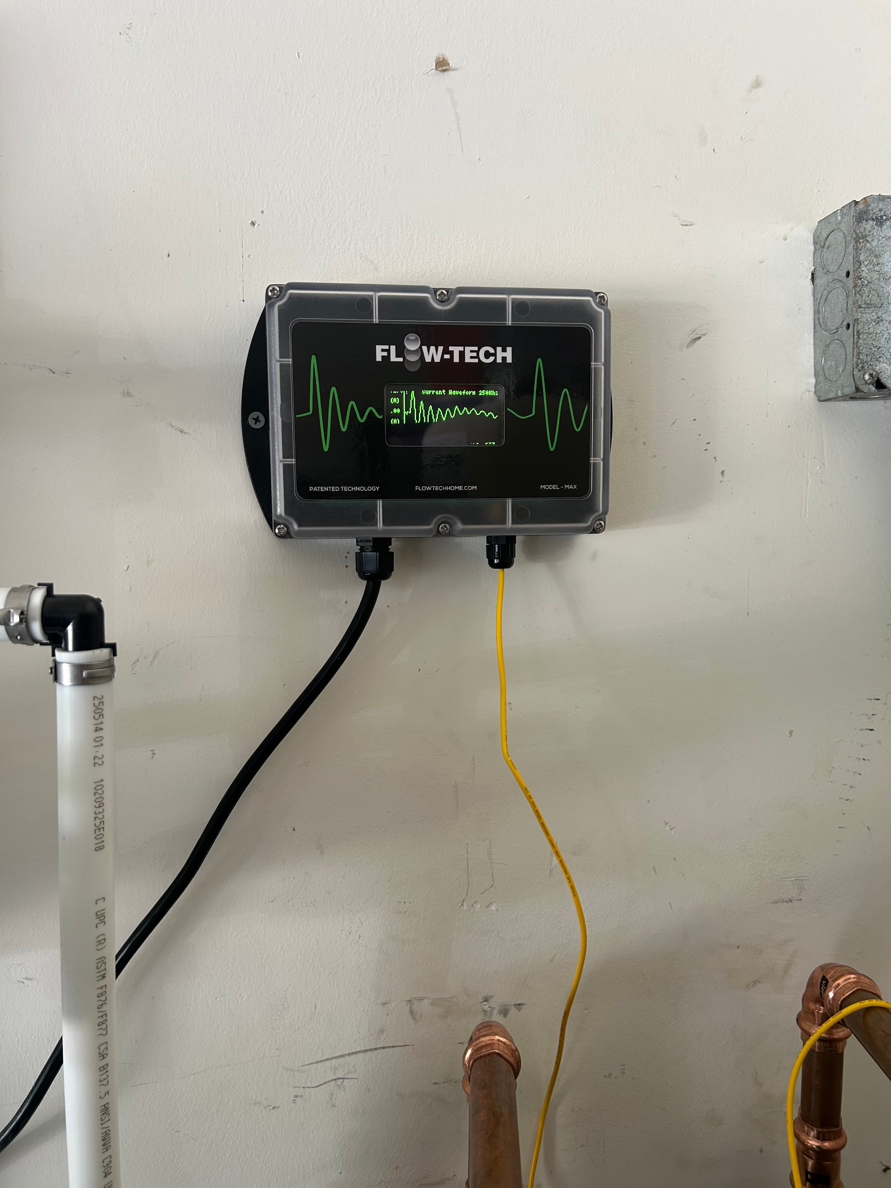 Flow-Tech water treatment device mounted on a wall with a screen displaying a green waveform.